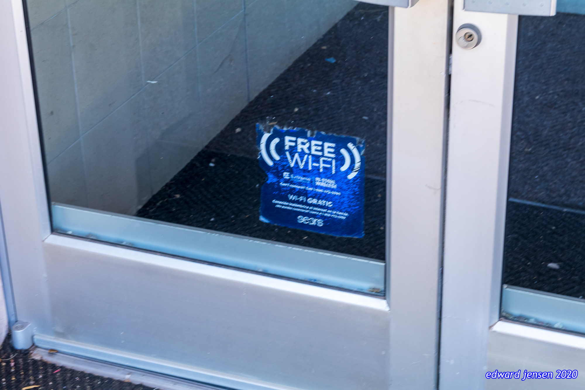 A glass door or window with a blue "FREE WI-FI" sign visible through it. The sign includes additional small text about Wi-Fi service.